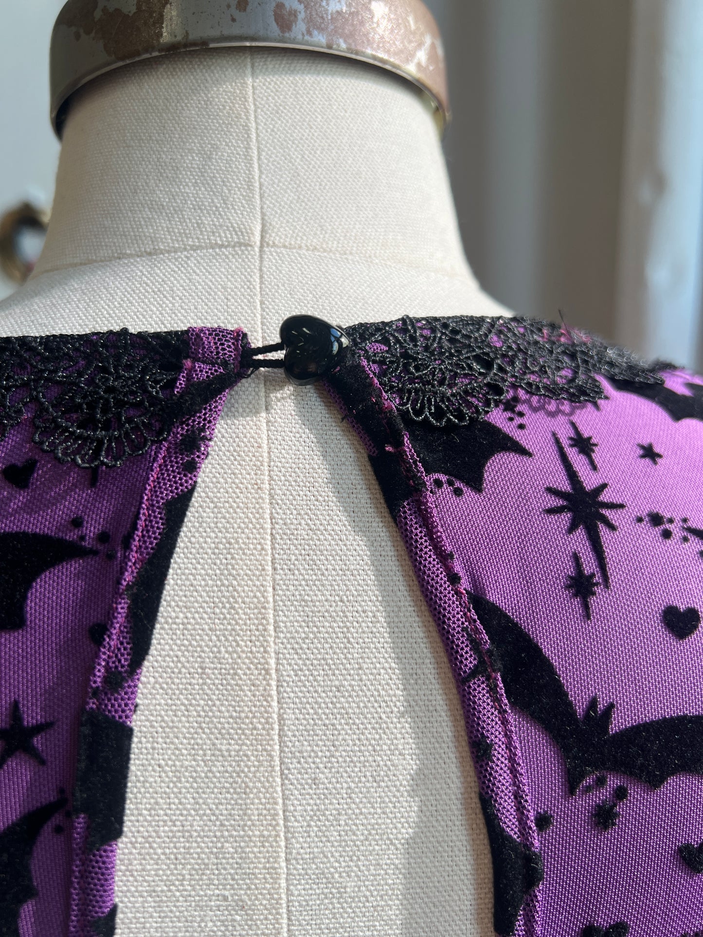 Back keyhole of the Raven Dress in Potion Purple with lace trim and dainty heart button, showcasing flocked bats and stars.