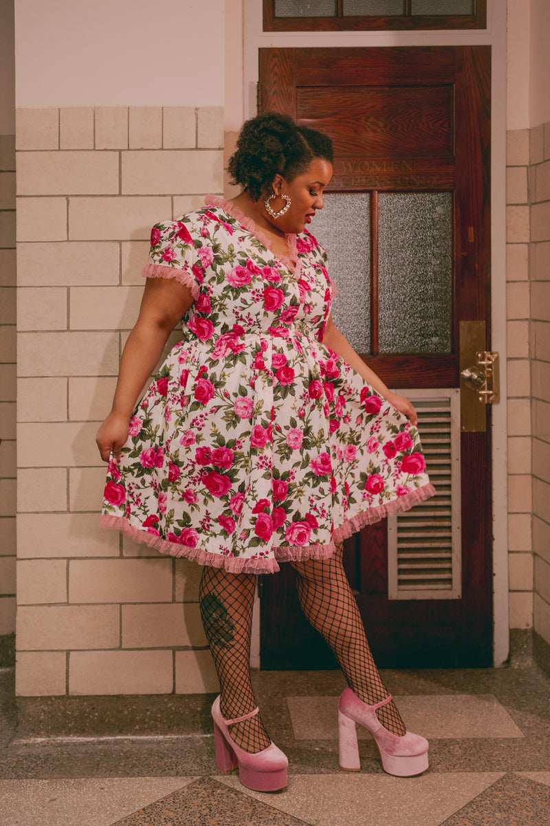 Plus size model twirling in a cotton floral dress with pink rose buttons and tulle trim, showcasing its pockets.