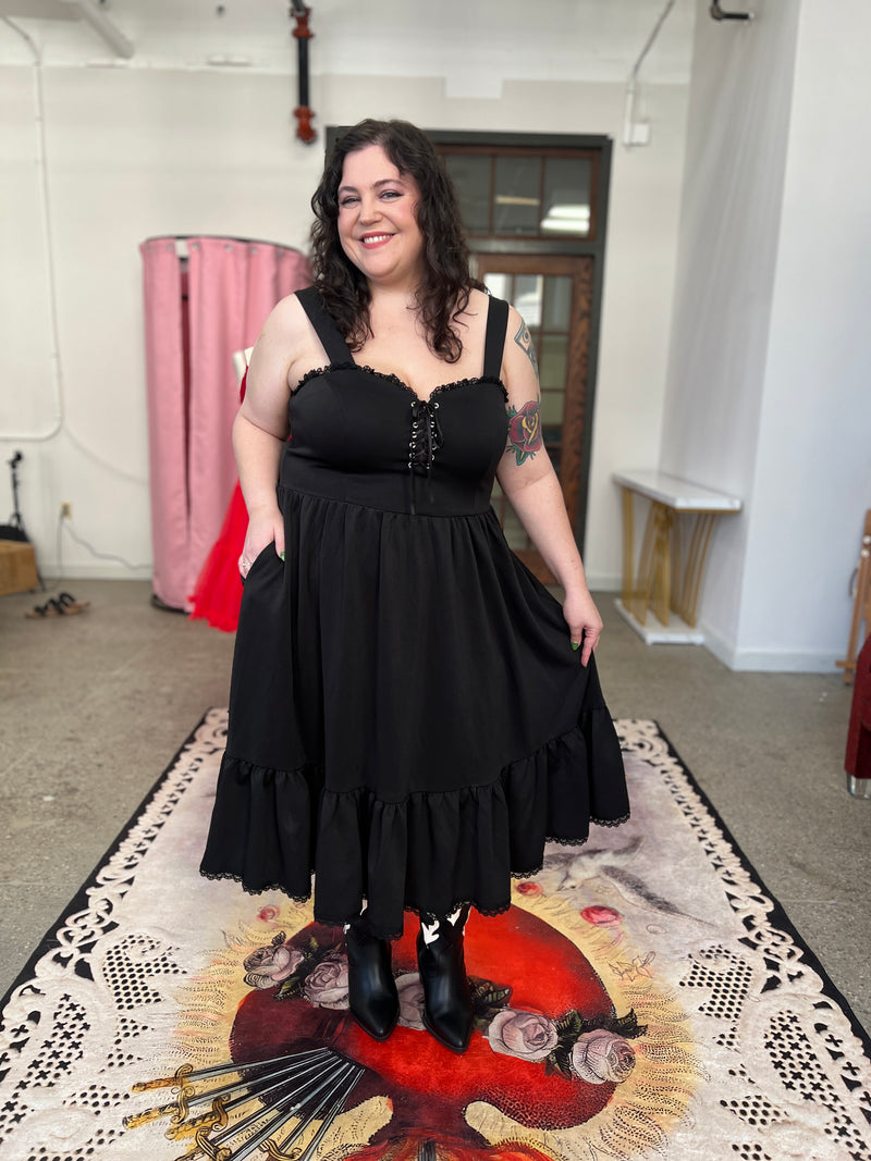 Model in black ponte swing dress with lace-up front, ruffles, and pockets, showcasing plus-size fashion.