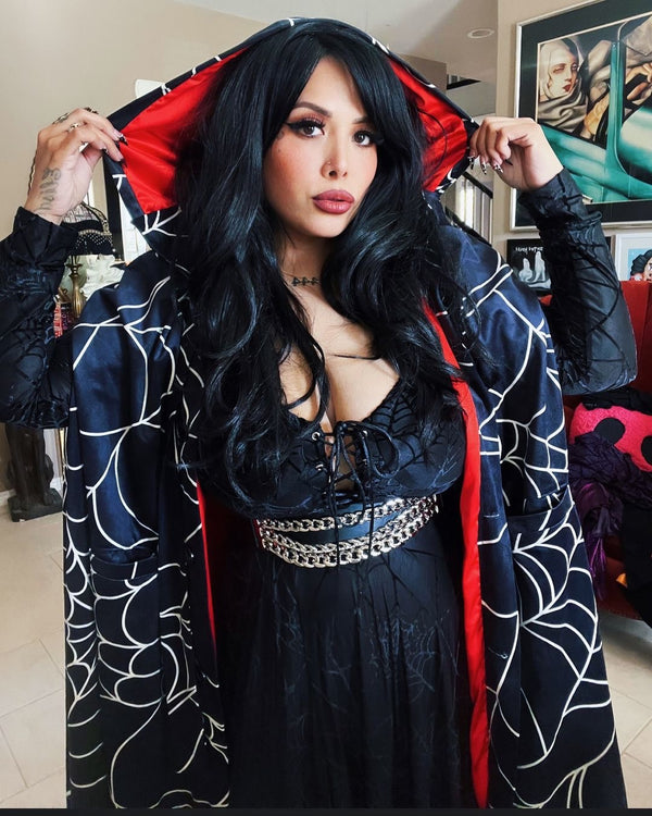 Model showcasing Florence Hooded Cape with spiderweb print, featuring red satin lining and oversized hood, exuding a cozy goth vibe.