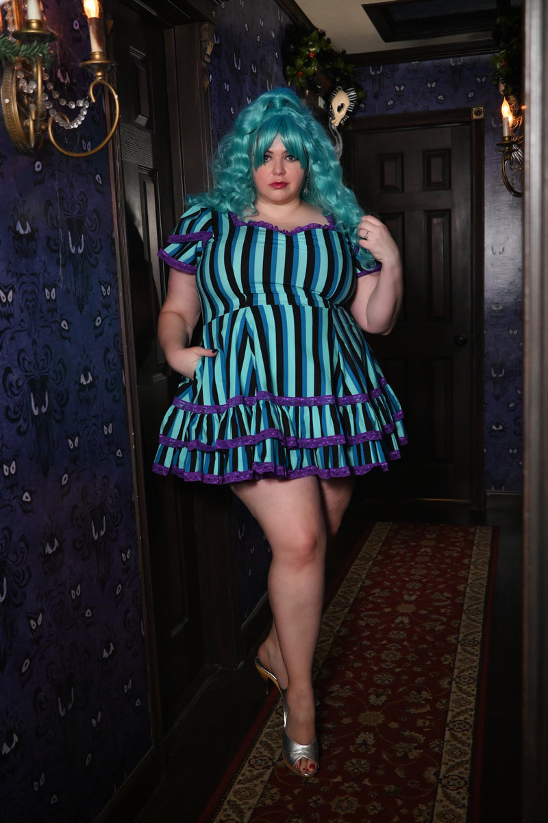 Plus size model in Adelaide Mini Swing Dress with purple lace trim, showing off pockets in Haunted Stripe pattern in spooky hallway.