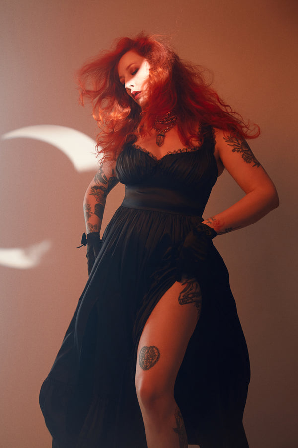 Model wearing the Cosette Maxi Dress in Jet Black, featuring thigh-high slits and lace detail, embodying a gothic romantic style.