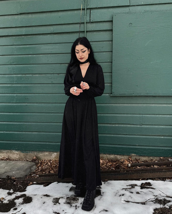 Model in a black brushed knit Raquel Maxi Dress with bishop sleeves standing against a green wall.