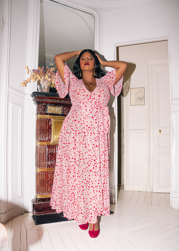 Model in pink mesh maxi wrap dress with red flocked hearts, showing elegant fit with pockets, perfect for Valentine's Day.