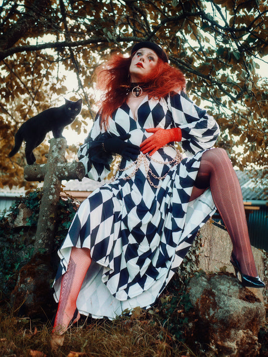 a model wearing a long black and white harlequin dress in a graveyard witha black cat