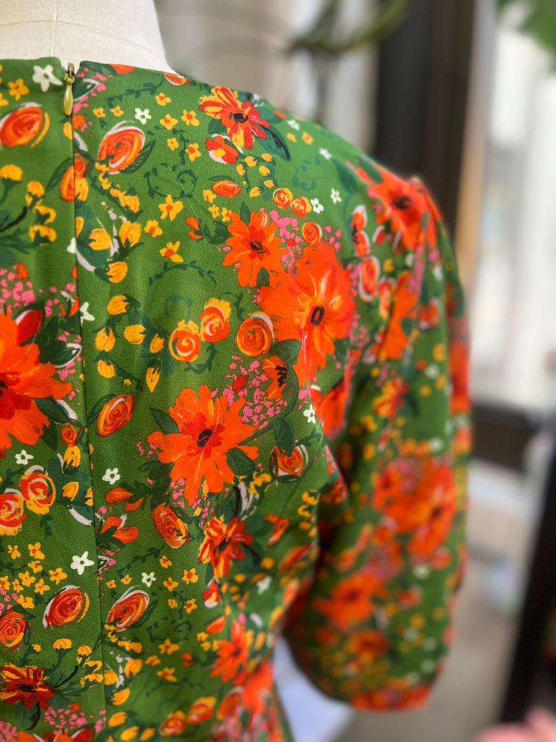 Back view of Penny Dress featuring vintage floral print in bright colors and bishop sleeves on green background.