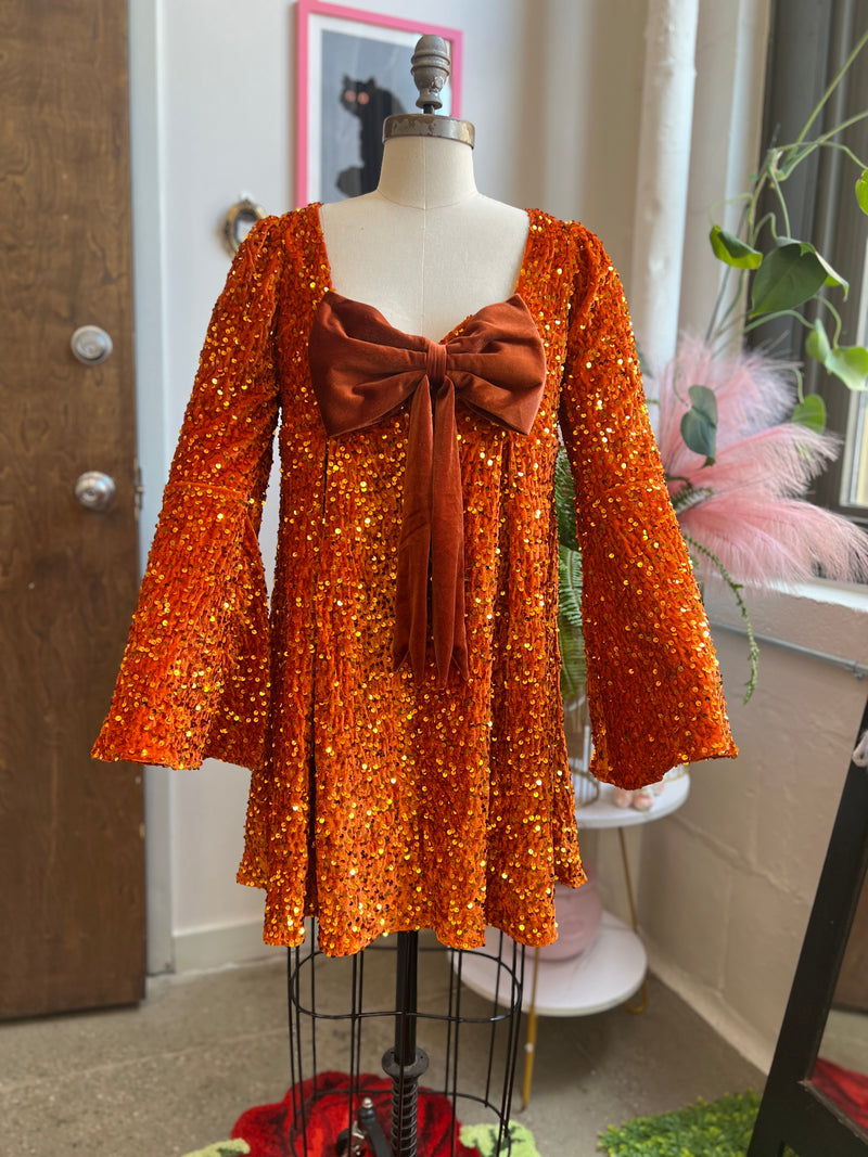 Priscilla 60's Mini Dress in pumpkin orange sequin velvet with bell sleeves and removable bow, perfect for Halloween.