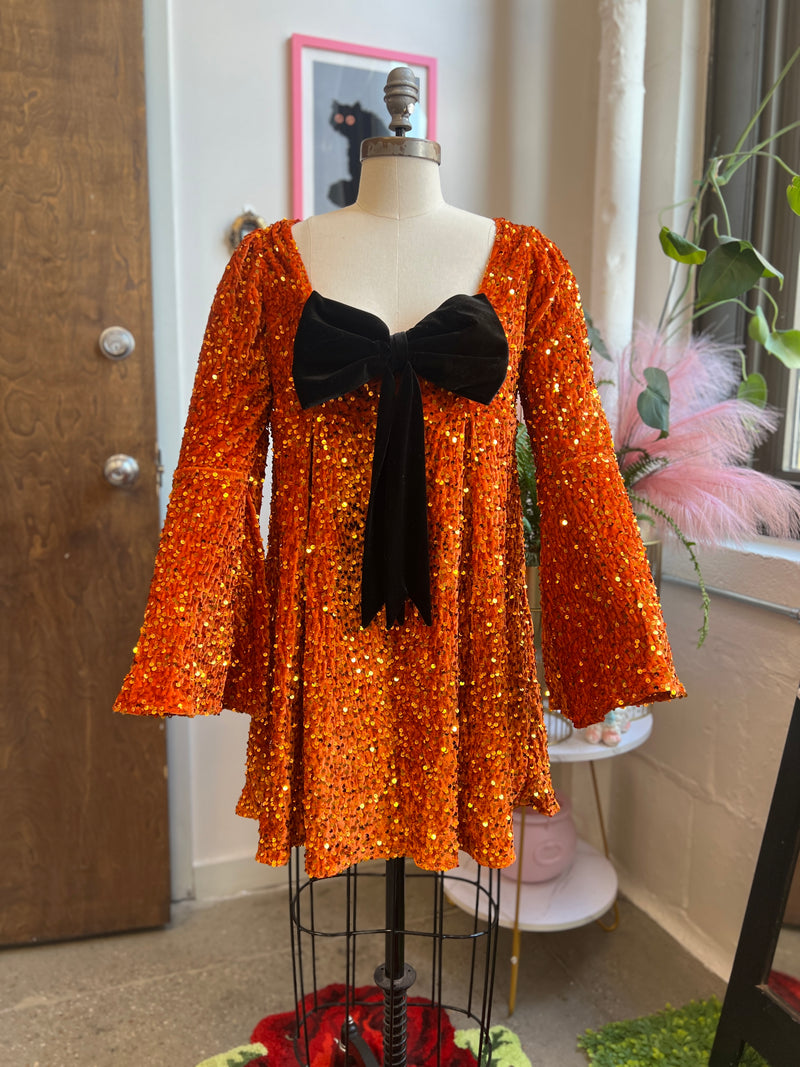 Priscilla 60's Mini Dress in orange sequin velvet with bell sleeves and removable black bow, perfect for Halloween.