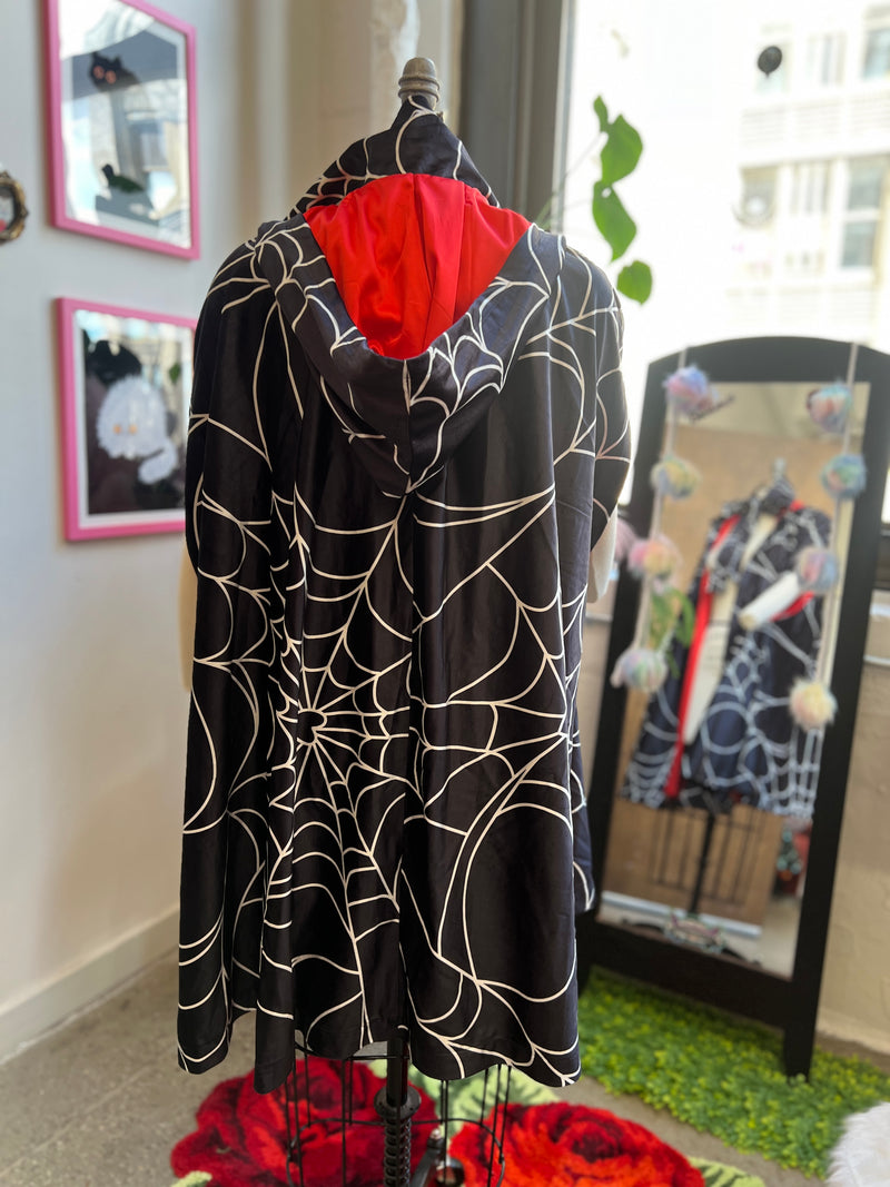 Florence Hooded Cape in spiderweb print with red satin lining, showcasing oversized hood and deep pockets.