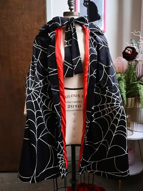 Florence hooded cape in spiderweb print with red satin lining, oversized hood, and deep pockets for a cozy goth look.