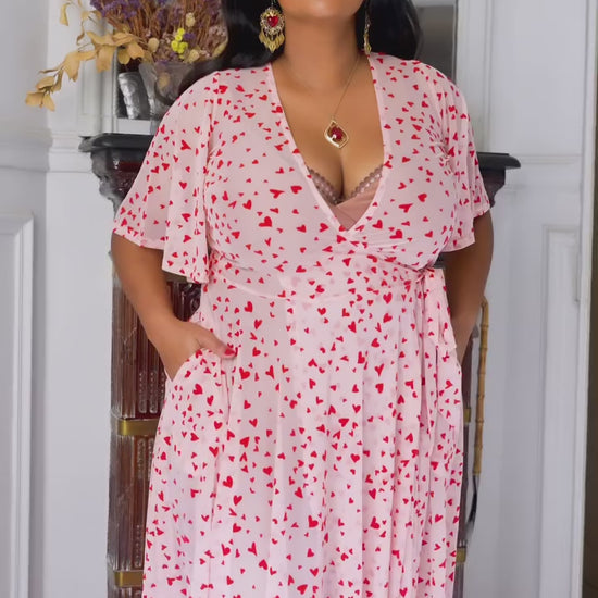 Model in pink mesh maxi wrap dress with flocked red hearts and pockets, perfect for Valentine's Day.